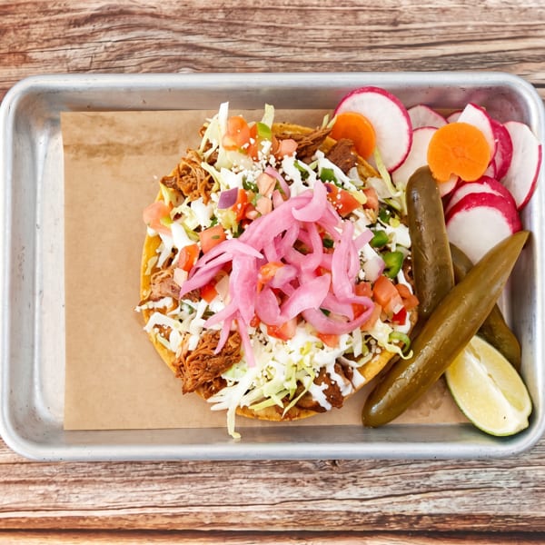 Tostada with shredded meat, cabbage, pico de gallo, pickled onions, and crema, served with radishes and jalapeños.