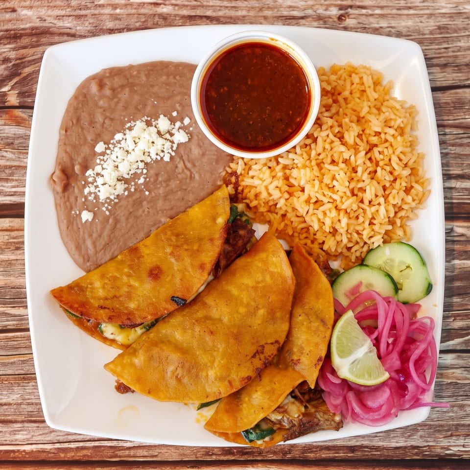 Three golden-fried tacos, rice, refried beans, and a side of red sauce on a white plate.