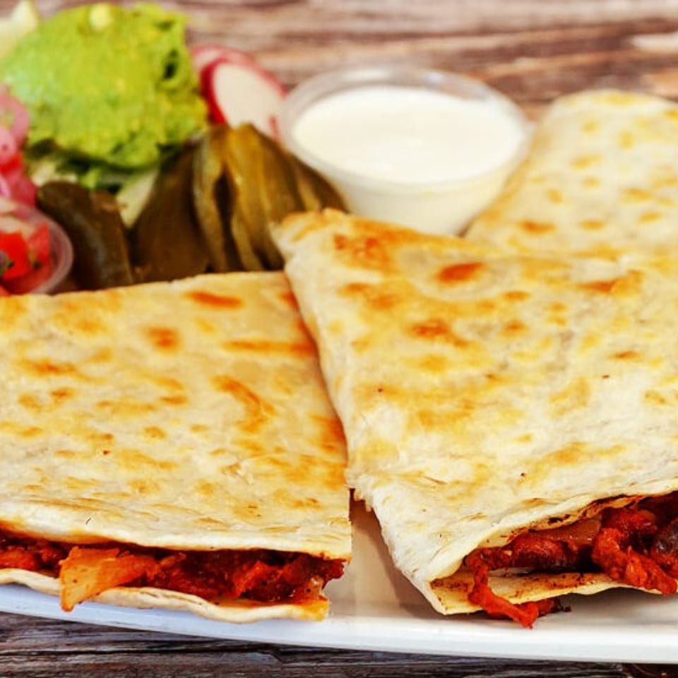 Three quesadillas with red meat filling, served with guacamole, salsa, sour cream, and pickled vegetables.
